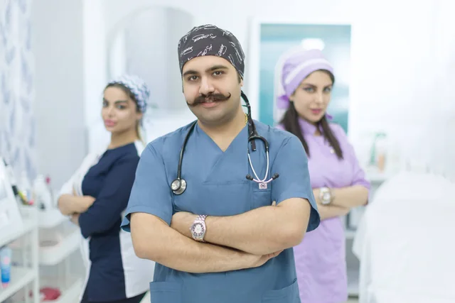 دکتر سعید قزلباش با لباس پزشکی و گوشی پزشکی، همراه اعضای تصویر گروهی در کرمانشاه